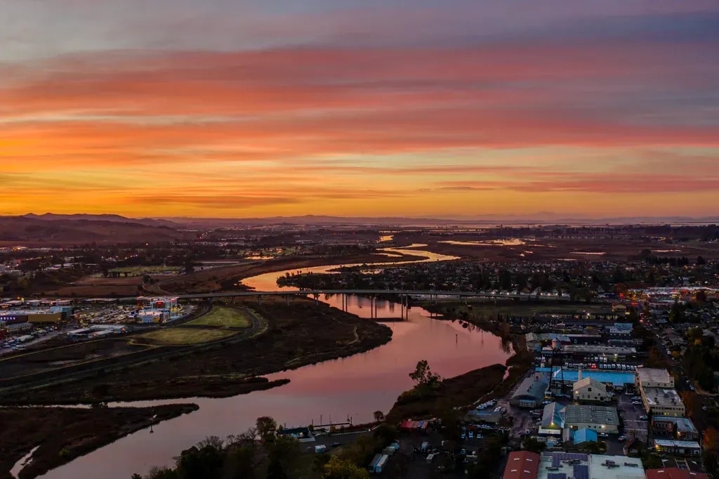 The Napa River at dusk from the air, winding under a highway bridge and through town, Napa, California
