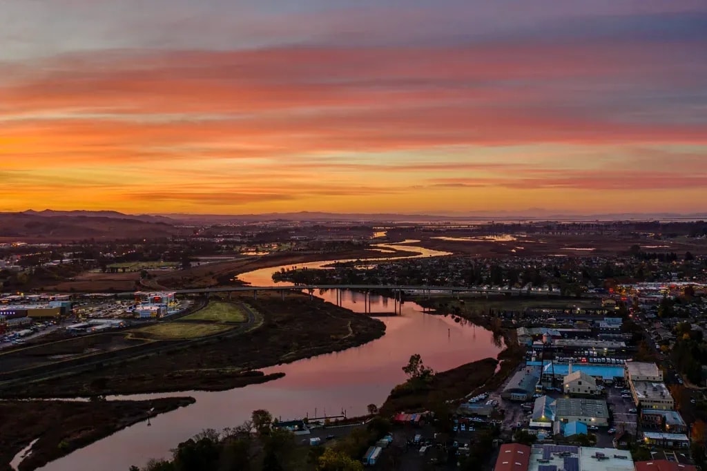 The Napa River at dusk from the air, winding under a highway bridge and through town, Napa, California