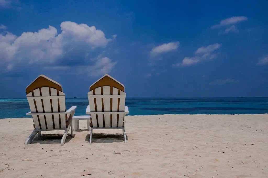 Two beach chairs on powder-white sand facing the turquoise water of the Maldives