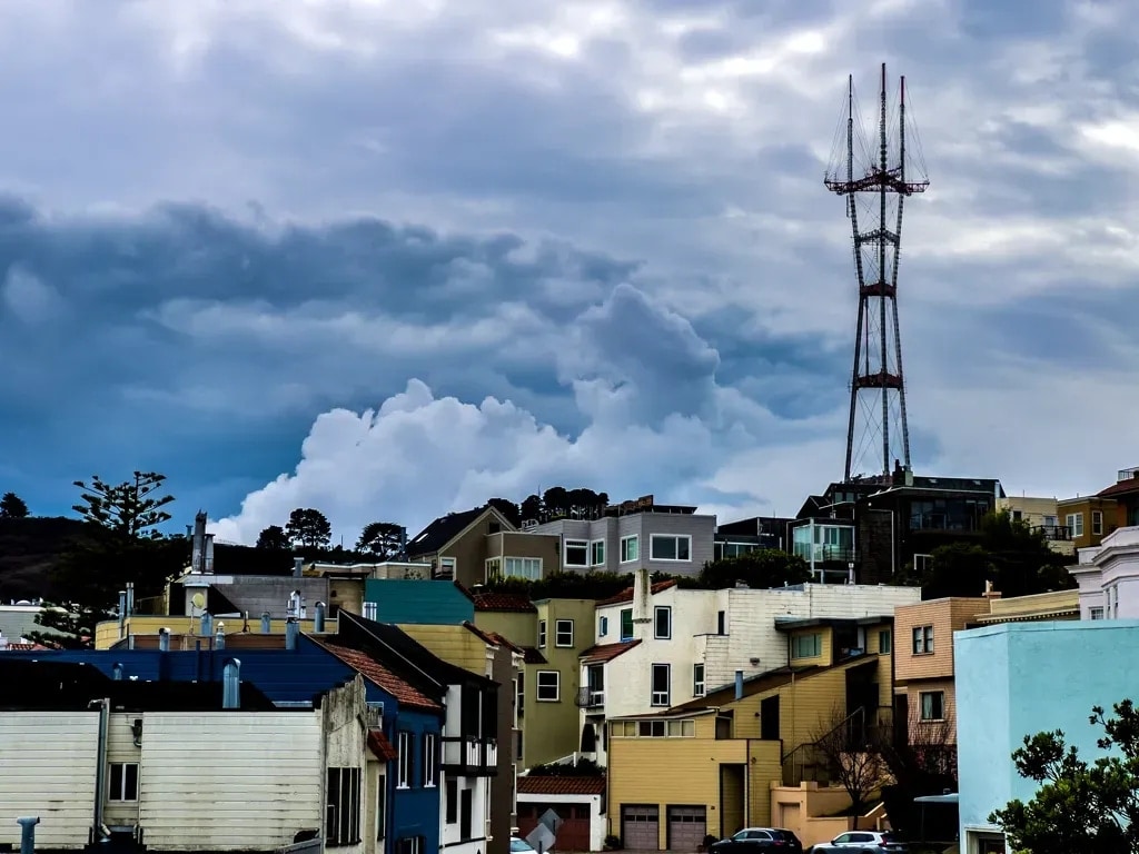 Sutro Tower rising above colorful hillside houses under heavy clouds, San Francisco